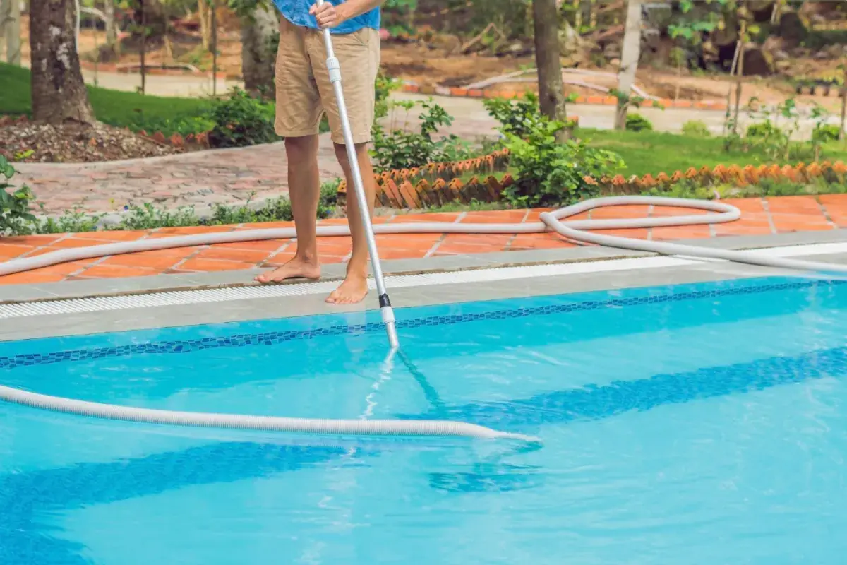 Profissional aspirando o fundo de piscina de água azul e cristalina